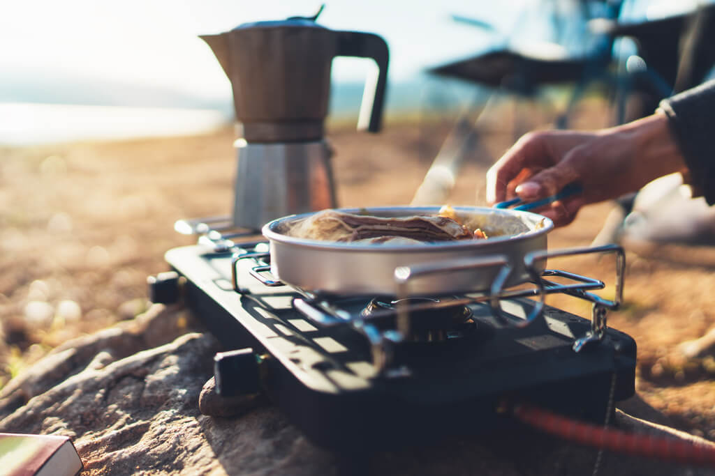 person preparing breakfast on a camp stove, easy camping breakfast ideas