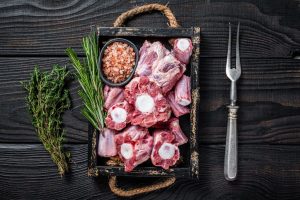 Tray of raw beef and veal oxtail, with a small bowl of salt, rosemary, and thyme sprigs
