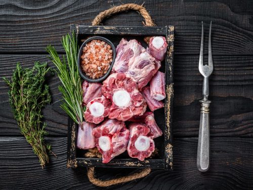 Tray of raw beef and veal oxtail, with a small bowl of salt, rosemary, and thyme sprigs 