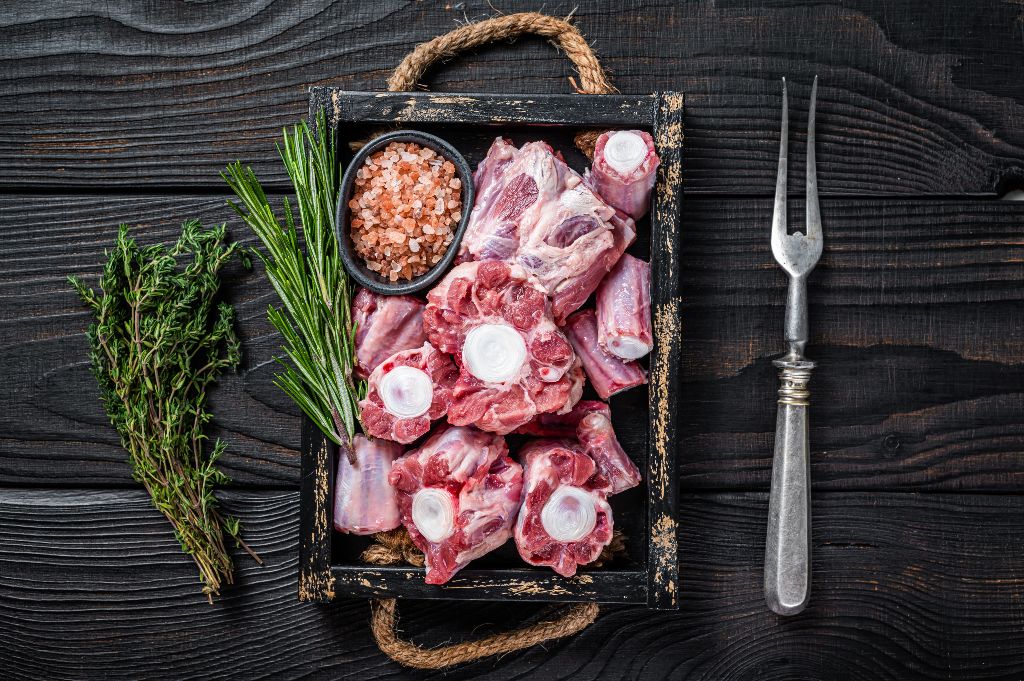 Tray of raw beef and veal oxtail, with a small bowl of salt, rosemary, and thyme sprigs 