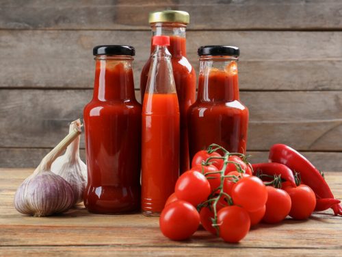 bottles with tasty tomato sauces and on wooden table, substitute for tomato sauce