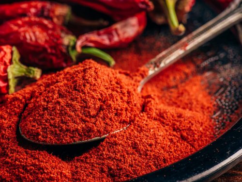 a spoonful of ground chili pepper and dried red chili pepper on a plate