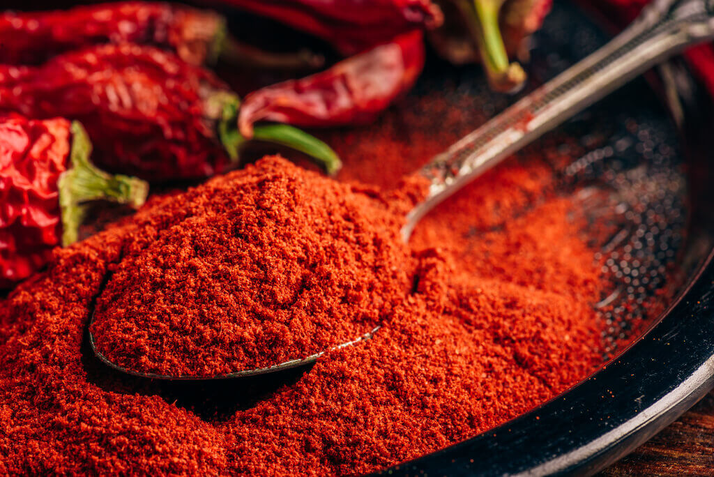 a spoonful of ground chili pepper and dried red chili pepper on a plate