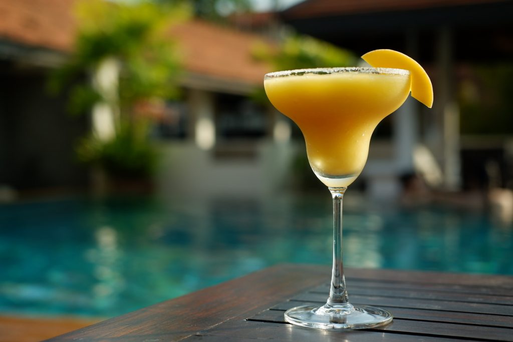 Frozen mango daiquiri decorated w a slice of mango with a pool background