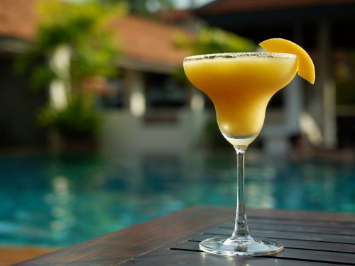 Frozen mango daiquiri decorated w a slice of mango with a pool background