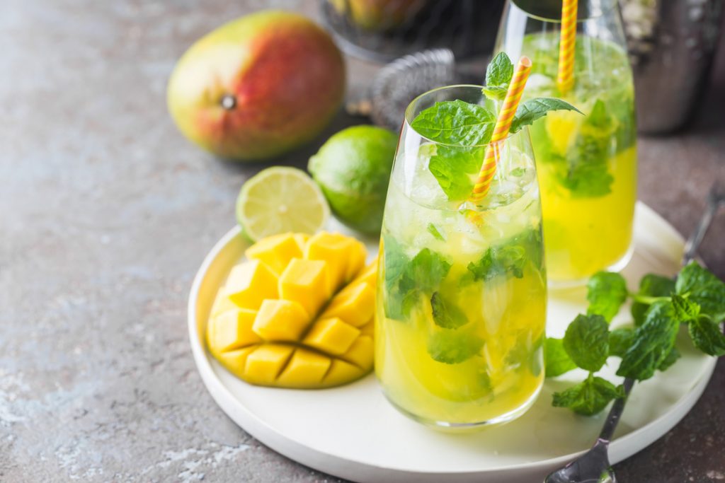 Fresh mango mojito cocktail with lime and mint in a glass on a white tray