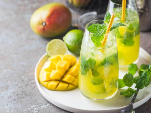 Fresh mango mojito cocktail with lime and mint in a glass on a white tray