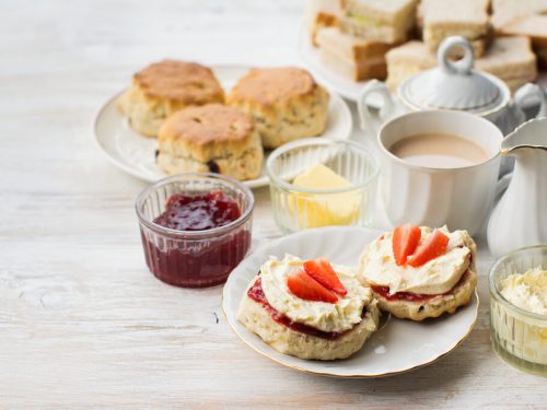 tea party food, English cream teas, scones with jam and cream, tea with milk, with sandwiches on the back, on the white wooden table