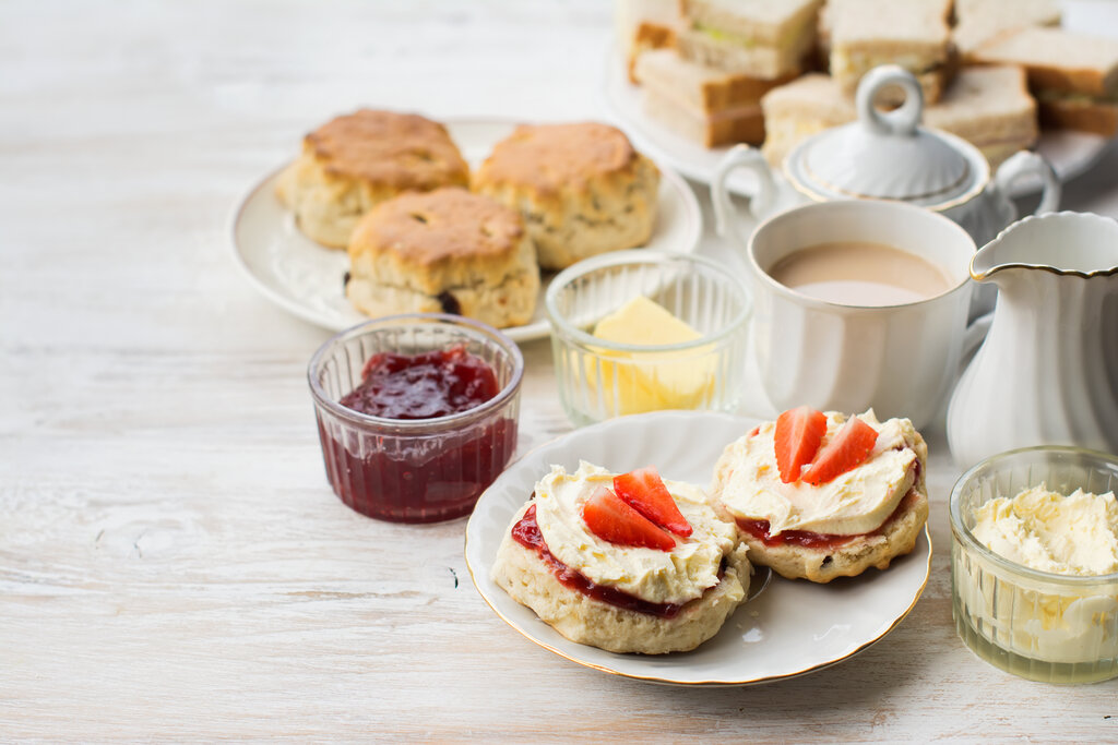 tea party food, English cream teas, scones with jam and cream, tea with milk, with sandwiches on the back, on the white wooden table