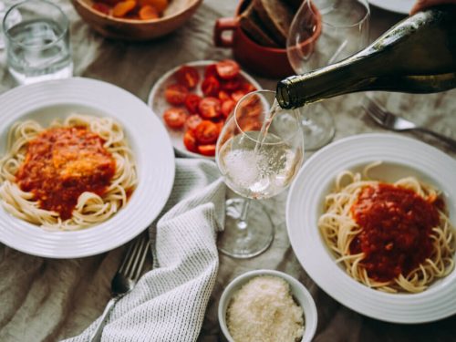 Dinner date with two plates of spaghetti and a person pouring wine in a glass.