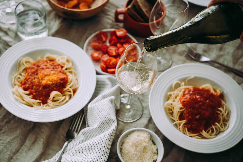 Dinner date with two plates of spaghetti and a person pouring wine in a glass.