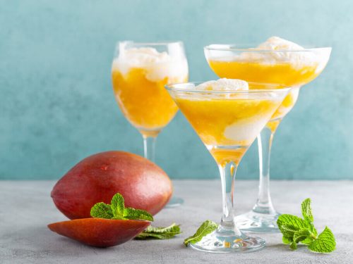 Mango cocktails topped with ice cream beside a mango fruit and mint leaves.