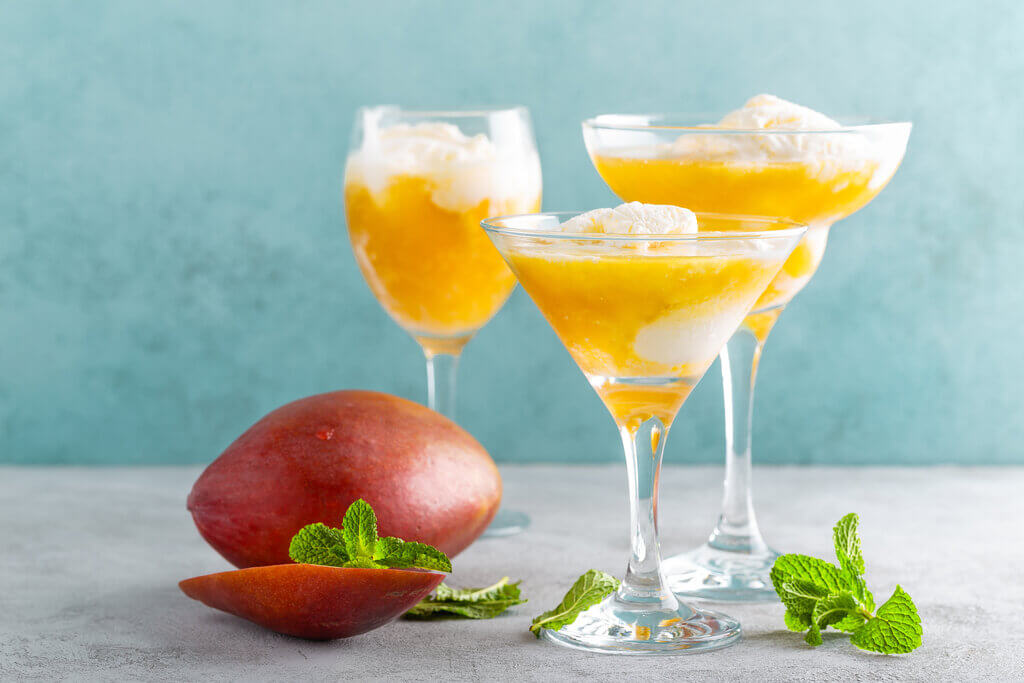 Mango cocktails topped with ice cream beside a mango fruit and mint leaves.