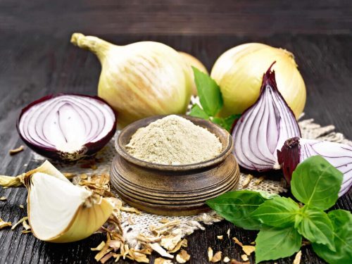onion powder in a bowl and fresh onion on dark wood