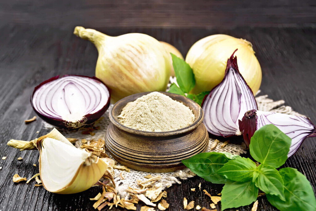 onion powder in a bowl and fresh onion on dark wood