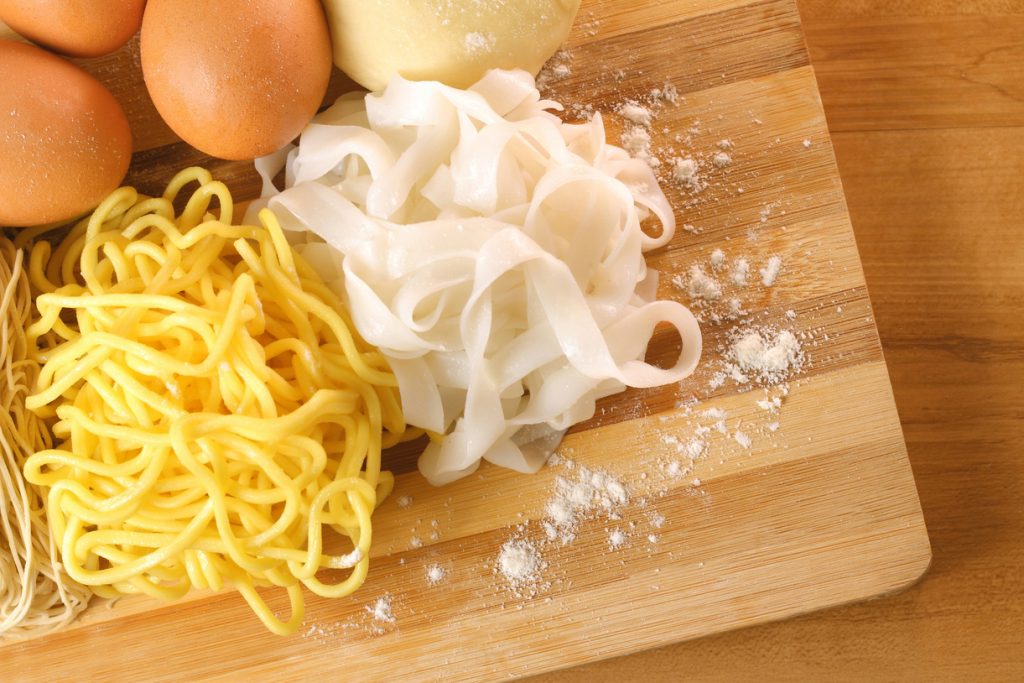 rice noodles vs egg noodles, freshly made and placed on a wooden board
