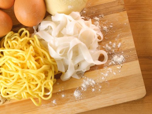rice noodles vs egg noodles, freshly made and placed on a wooden board