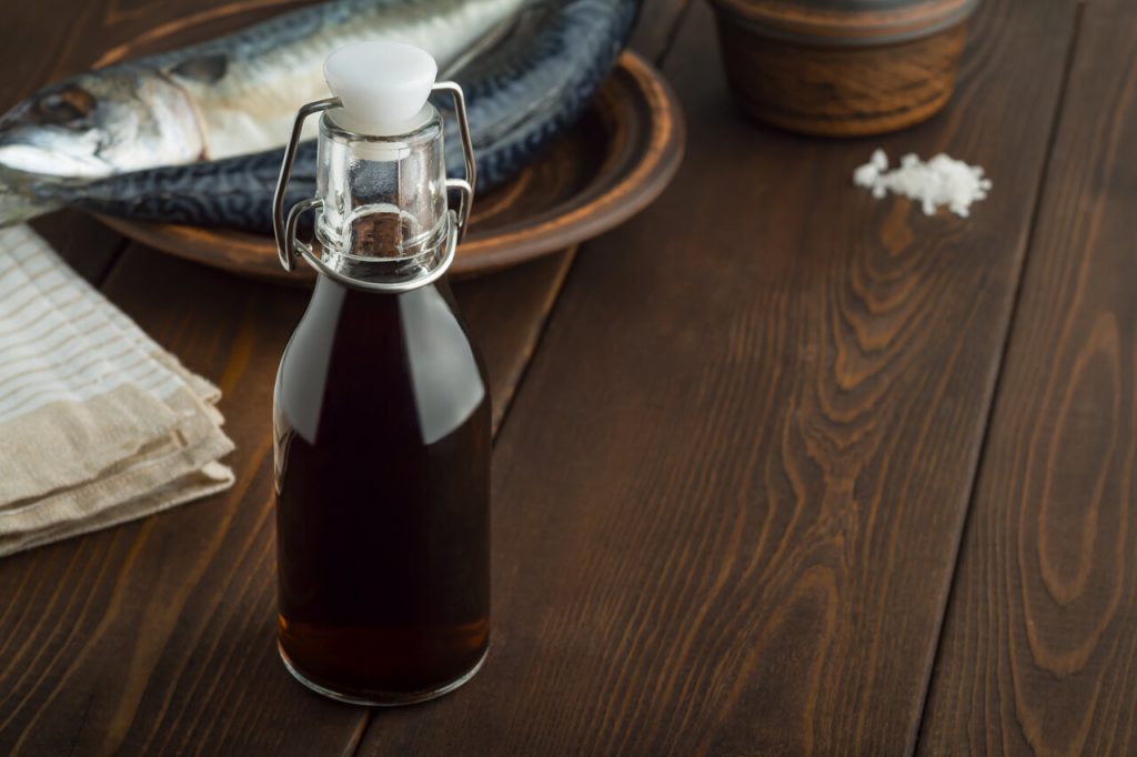 a bottle of fish sauce with a plate of fish in the background