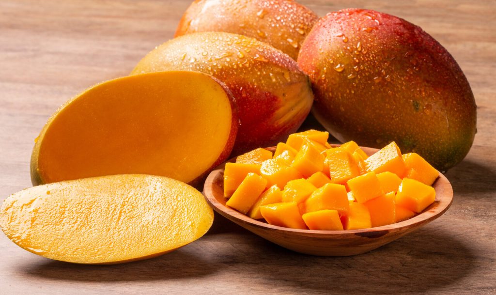 a plate of sliced mango beside whole ripe mangoes, how to cut a mango