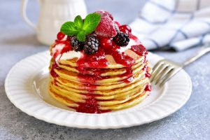 stack of pancakes topped with sour cream, raspberry syrup, and berries