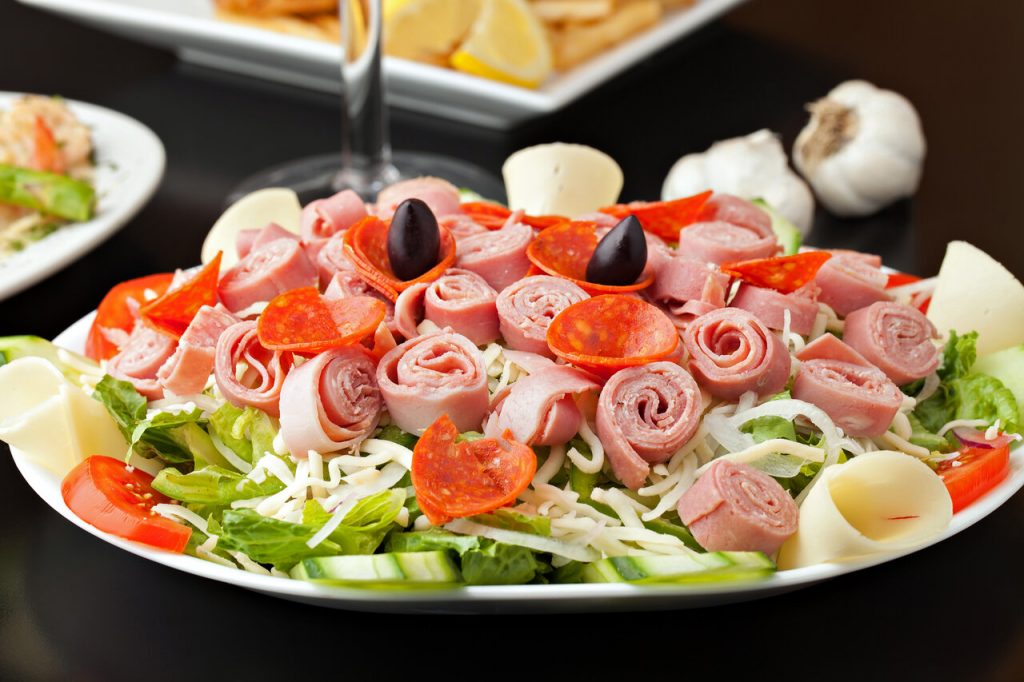 Antipasto Salad Recipe, Antipasto salad topped with meats and olives on white plate with black background