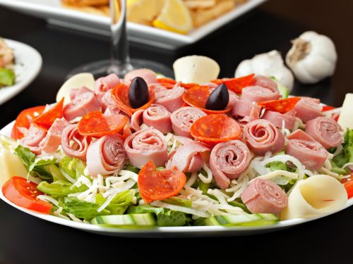 Antipasto Salad Recipe, Antipasto salad topped with meats and olives on white plate with black background