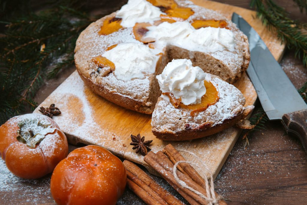 Persimmon Cake Recipe, Persimmon cake topped with whipped cream and powdered sugar, served on wooden chopping board