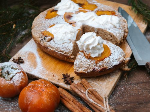 Persimmon Cake Recipe, Persimmon cake topped with whipped cream and powdered sugar, served on wooden chopping board