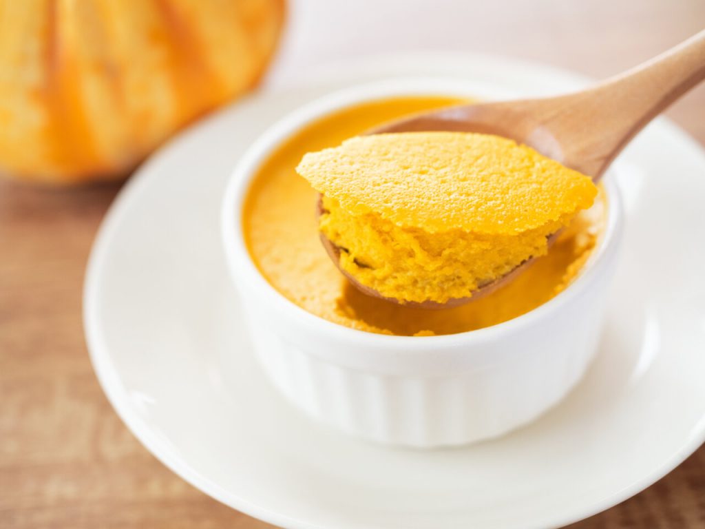 Persimmon Pudding Recipe, Persimmon pudding being scooped from ramekin using a wooden spoon