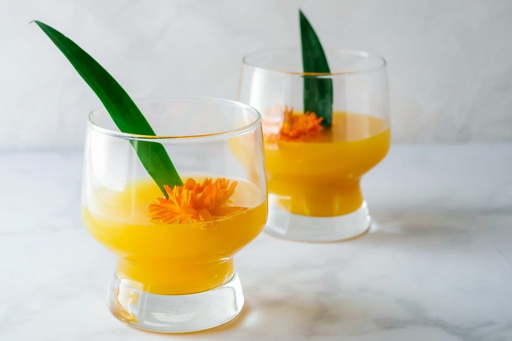 Two glasses of pineapple mango mimosa decorated with a leaf