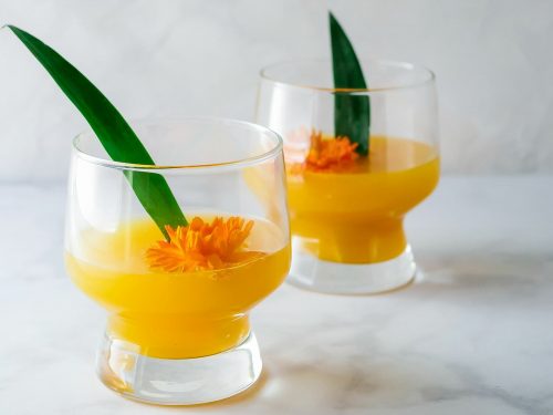 Two glasses of pineapple mango mimosa decorated with a leaf