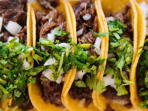 Sweet Pork Tacos Recipe - Tortillas stuffed with slow-cooked, shredded pork and topped with herbs and minced white onions.